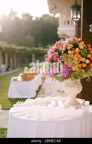 Ricevimento con tavolo da pranzo per matrimoni. Un bouquet enorme in un antico vaso di marmo di rose rosa, rosse, arancioni e gialle, idrangee verdi, orchidee viola. Stand Foto Stock