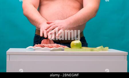 l'uomo con una pancia grassa sceglie tra salsiccia e mela verde. Il concetto di dieta e di volontà. Foto Stock