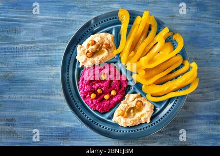 Primo piano su piatto blu colorato con bastoncini di paprika giallo e bagno hummus di barbabietola rossa Foto Stock