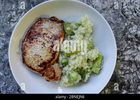 Carne arrosto e risotto con asparagi in piastra rotonda bianca su fondo di granito. Vista ad angolo alto. Foto Stock