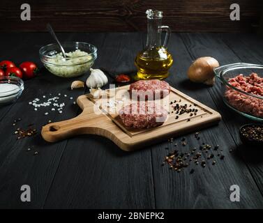 Cutlets di carne macinata con gli ingredienti sul tavolo di legno nero. Cucina casalinga. Foto Stock
