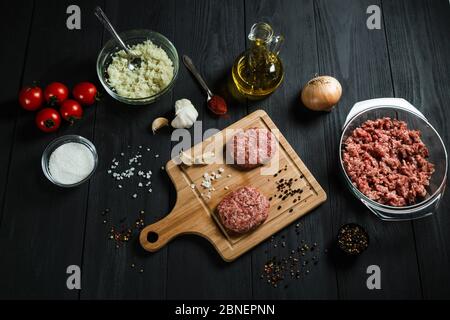 Cutlets di carne macinata con gli ingredienti sul tavolo di legno nero. Cucina casalinga. Foto Stock