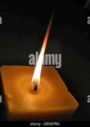 Immagine in primo piano verticale di una candela arancione quadrata con un concetto di sfondo scuro: Rilassante Foto Stock