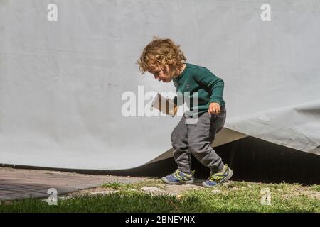 Carino colpo di biondo, riccia capelli bambino, che sale da sotto tenda. Foto Stock