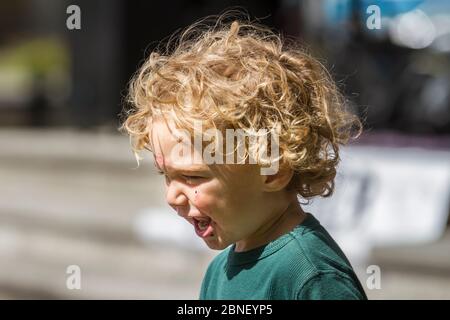 Cute testa shot di biondo, riccia capelli bambino. Il viso è disordinato con la torta. Foto Stock