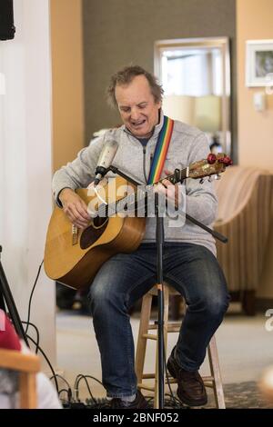 Foto di un maschio anziano, suonando la chitarra e cantando, sembra divertirsi. Shot verticale. Foto Stock