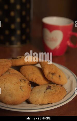 Immagine verticale in cui i biscotti fatti in casa sono visti accanto a una tazza rossa di caffè con un cuore inscritto sulla sua superficie Foto Stock