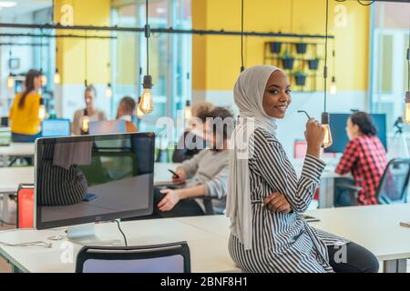 Protarit di una donna musulmana nera (afro-americana) in piedi in un moderno ufficio d'affari mentre indossa un hijab. Foto Stock