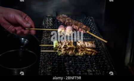 Grigliare deliziosi yakitori del supporto per alimenti. Appetitosi spiedini di pollo alla griglia a Tokyo. Piatti spiedati in stile giapponese nel ristorante izakaya. Foto Stock