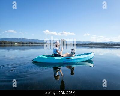 Giovane donna e cane kayak sul lago tranquillo e soleggiato, i migliori amici, isolamento calma e concetto di pace Foto Stock