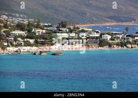 Proprietà e spiagge a Camps Bay, Città del Capo, Sud Africa in una giornata estiva limpida, con persone sulla spiaggia e le montagne sullo sfondo Foto Stock