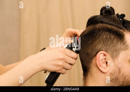 Rasoio elettrico per taglio di capelli maschile. La mano del parrucchiere rasa i capelli con il rasoio elettrico. Hipster man ottenere un taglio di capelli trendy con un regolacapelli e pettine. Servizi Barbiere. Procedura di acconciatura. Foto Stock