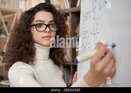 Giovane insegnante di matematica latina che indossa occhiali che scrivono sulla lavagna Foto Stock