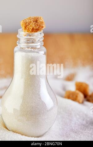 Vaso di zucchero bianco con cubetti gialli su tavola di legno, che suggerisce un concetto di dieta e salute. Foto Stock