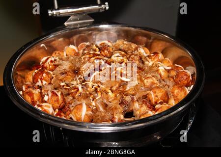 Ampia porzione di cibo giapponese di strada, Takoyaki, con fiocchi di bonito secchi sulla parte superiore in un vassoio a buffet Foto Stock