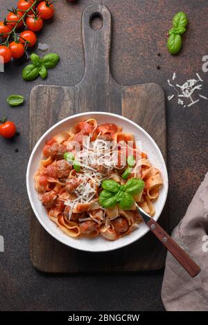 Fettuccine di pasta italiana fatta in casa con polpette, formaggio, pomodori, basilico su tavola marrone. Vista dall'alto. Formato verticale. Foto Stock