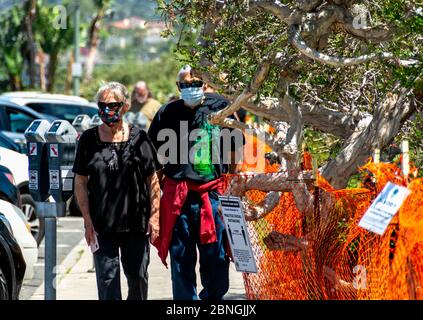 Una coppia senior, con maschere, cammina lungo il marciapiede di fronte a un parco cittadino, chiuso a causa del COVID-19. Barriere e cartelli temporanei. Foto Stock