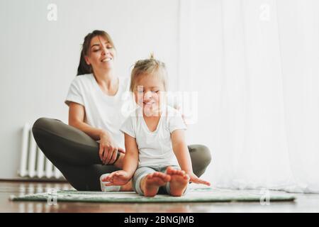 Mamma felice e bambina che fanno yoga mattina esercizio insieme a casa luminosa interno Foto Stock