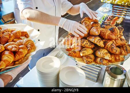 Mani in guanti bianchi di due piatti, uno dei quali stende croissant su un piatto e l'altro contiene un piatto con croissant Foto Stock