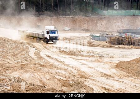 GRODNO, BIELORUSSIA - APRILE 2020: Camion pesante multi-ton MAZ cabina bianca e carrozzeria grigia arriva al cantiere caricato con cemento armato Foto Stock