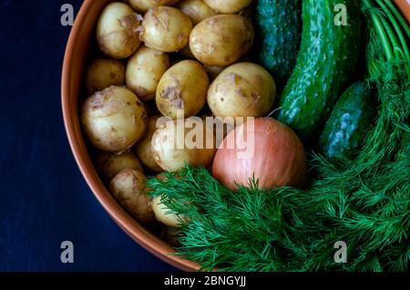 Verdure raccolte di fresco in una ciotola di creta. Aneto, cetrioli, patate e cipolle. Verdure self-grown. Vista dall'alto. Primo piano. Foto Stock