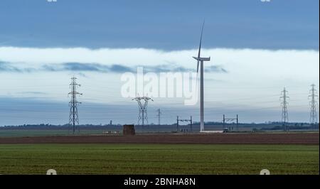 Una singola turbina eolica sul campo con tralicci elettrici sullo sfondo Foto Stock