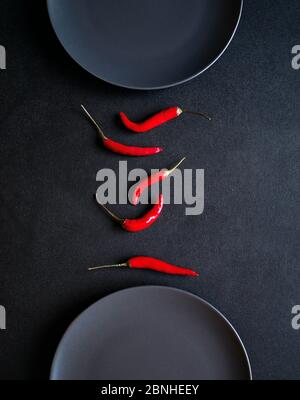 Composizione minimalista di peperoncini rossi tra due piatti in ceramica al tavolo nero Foto Stock