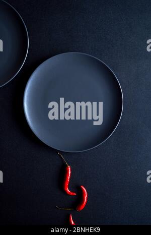 Composizione minimalista di peperoncini rossi e due piatti in ceramica su sfondo nero Foto Stock