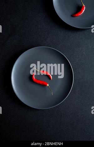 Composizione minimalista di due peperoncini rossi in ceramica nera al tavolo nero Foto Stock