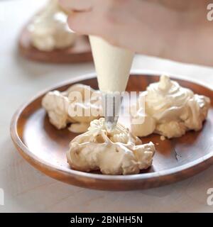 Il processo di creazione di Pavlova dessert, decorazione della meringa con crema Foto Stock