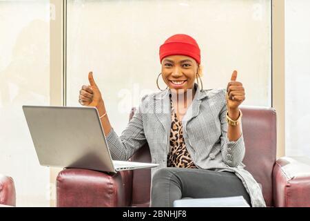 bella giovane donna d'affari musulmana africana che usa il suo computer portatile sorridendo e dando pollici in su Foto Stock