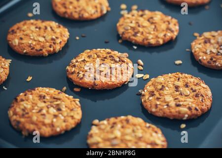 Farinata d'avena fatta in casa, biscotti con semi deliziosi giacciono su una teglia scura. Cucina casalinga. Foto Stock