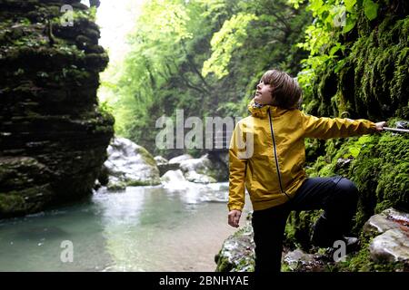 Ragazzo in giacca gialla che cammina attraverso la gola del fiume tenendo una corda di sicurezza alla cascata di Kozjak, Slovenia Foto Stock