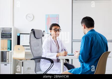 Donna medico che discute con paziente la sua malattia mentre si siede al tavolo durante la sua visita in ospedale Foto Stock