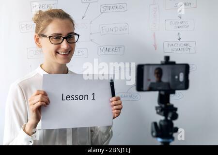 formazione online, webinar e business vlog concept - insegnamento donna e registrazione video con telefono davanti a lavagna bianca Foto Stock
