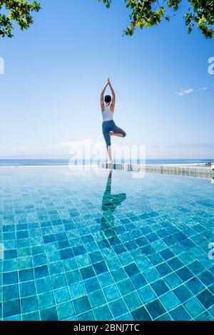 Una giovane donna che pratica yoga accanto a una piscina infinity, Candidasa, Bali, Indonesia, Sud-Est asiatico, Asia Foto Stock