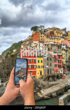 Prospettiva personale di un uomo che fotografa Riomaggiore con smartphone, cinque Terre, Sito Patrimonio dell'Umanità dell'UNESCO, provincia la Spezia, Liguria, Italia, E. Foto Stock