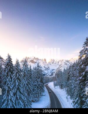 Veduta aerea con drone di auto viaggiando sulla strada panoramica Dobbiaco-Misurina lungo boschi innevati all'alba, Dolomiti, Alto Adige, Italia, Europa Foto Stock