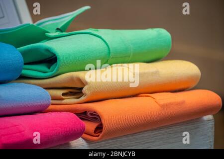 Un mucchio di camicie di polo in cotone in molti colori diversi, esposto in una vetrina. Foto Stock