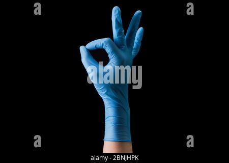 Mano del medico in guanti medici sterili in gesto di OK isolato su nero Foto Stock
