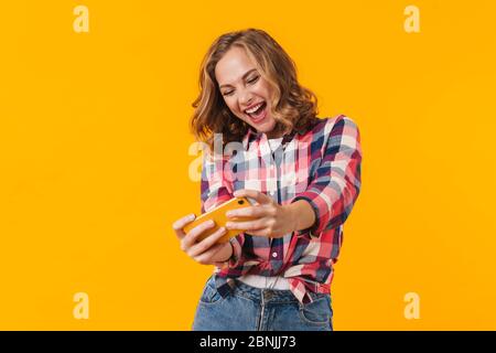 Immagine di giovane bella donna che indossa camicia plaid sorridente e tenendo il cellulare isolato su sfondo giallo Foto Stock