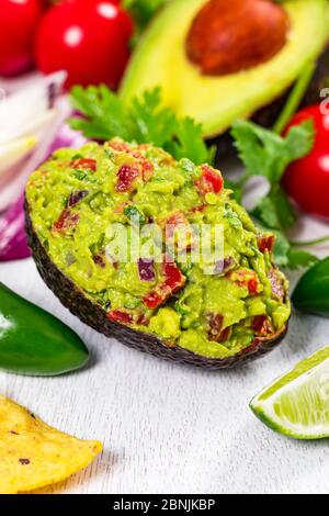 Guacamole immergersi in metà delle pelli di avocado su sfondo di legno bianco. Foto Stock