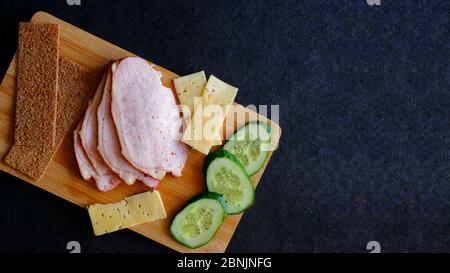 Prosciutto, cetrioli e formaggio affettati con pane di segala si trovano su una tavola di legno. Vista dall'alto con spazio per la copia Foto Stock