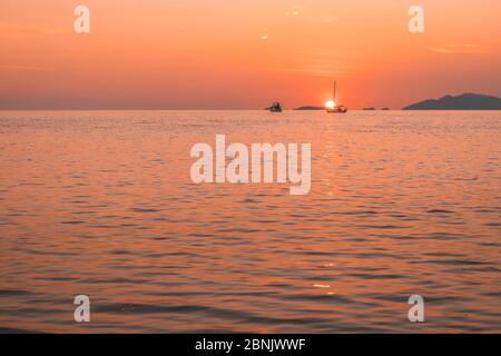 romantico tramonto in mare con barca a vela lungo il suo viaggio contro il cielo di colore arancione e giallo Foto Stock