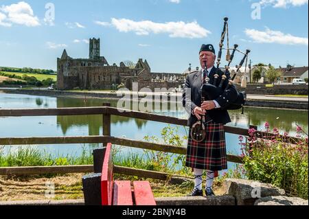 Timoleague, West Cork, Ireland. 15th May, 2020. Local man Michael Heaney from Timoleague plays the bagpipes with Timoleague Abbey in the background. Mr Heaney was filmed playing the pipes as part of Arigideen Rangers GAA Club's fundraising initiative. The GAA Club is raising money for Clonakilty Community Hospital, Pieta House and Timoleague Parish Church. Credit: AG News/Alamy Live News Foto Stock