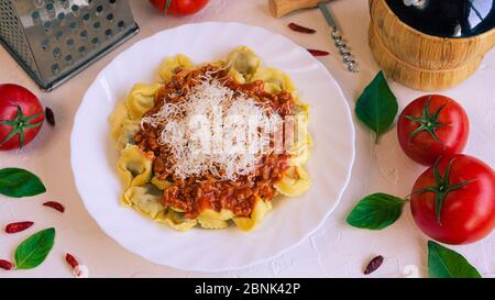 Un piatto pieno di pasta italiana accompagnata da pomodori, basilico e una bottiglia di vino moscato Foto Stock