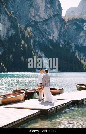 Gli sposi camminano lungo un molo di legno al Lago di Braies in Italia. Matrimonio in Europa, sul lago Braies. Gli sposi novelli camminano, baciano, abbracciano su un Foto Stock