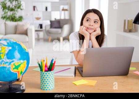 Foto di piccola scuola ragazza aspettare notebook lezione online conferenza mentalità pensare sopra vacanze estive tavolo seduta guardare sognante a distanza Foto Stock