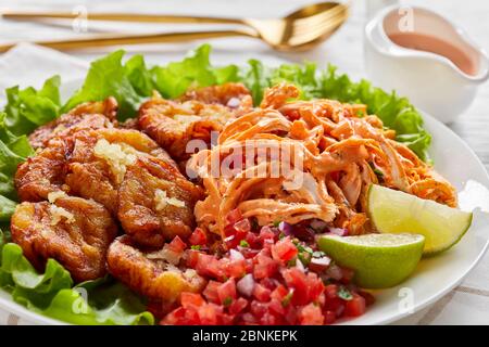 Piatti da asporto latinoamericani: Platani verdi fritti con aglio serviti con pollo tritato con salsa di bufalo e pico de gallo con lime su A. Foto Stock