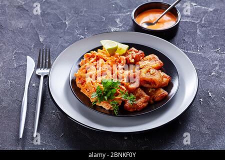 Piantine verdi fritte due volte fritte servite con pollo sminuzzato caricato con salsa di bufalo, con lime e prezzemolo su un piatto nero con posate, su un Foto Stock